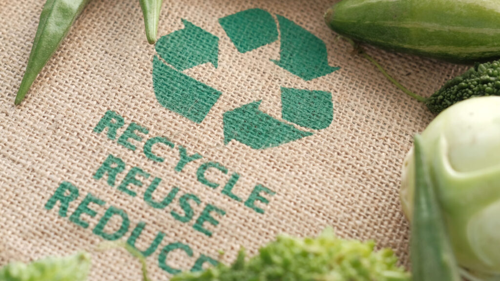 Recycle Reuse Reduce imprinted on a burlap bag framed in vegetables